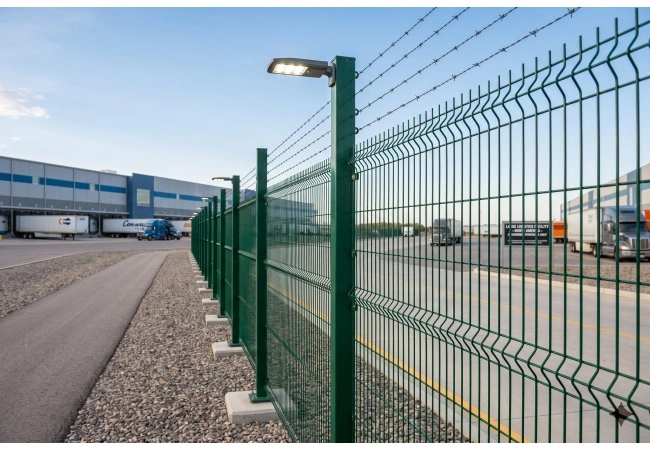 Tendenze delle recinzioni di sicurezza perimetrali commerciali 2026 Modern commercial perimeter security fence at logistics facility with integrated security lighting
